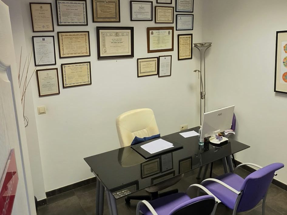 Despacho con mesa de consulta y títulos enmarcados en la pared