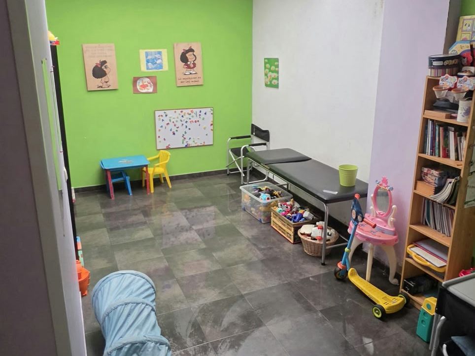Sala de psicomotricidad con pared verde, túnel de gateo, juguetes y mesa infantil